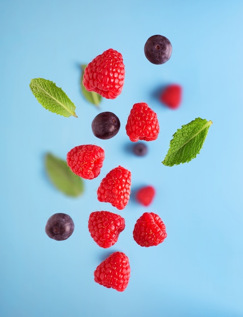 Flying berries on a blue table. Falling raspberry fruits and mint