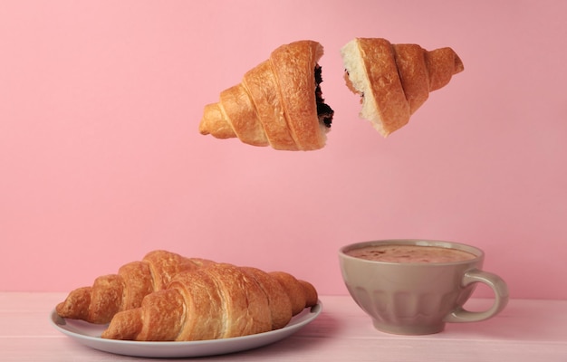 Flying croissant with coffee on pink background