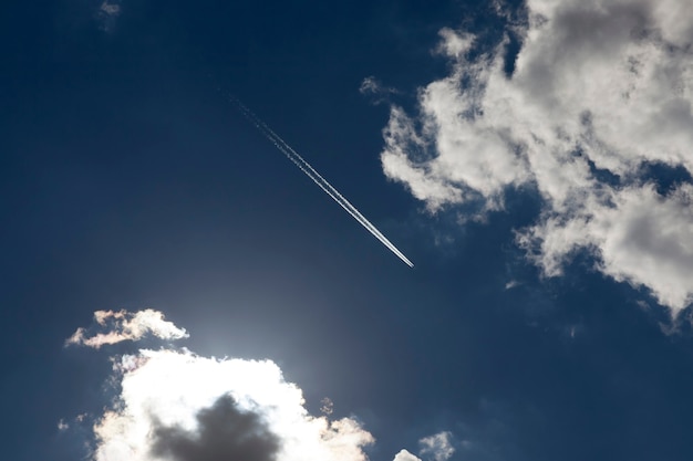 Flying high in the sky plane, behind which there was a white inversion trail from the engine, against a background of blue sky and white cumulus clouds