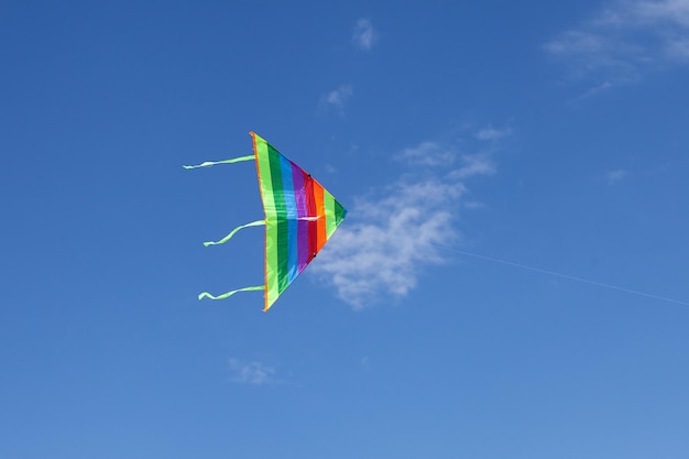 Flying kite Rainbow kite hovers in the air high in the sky. Blue sky with clouds.