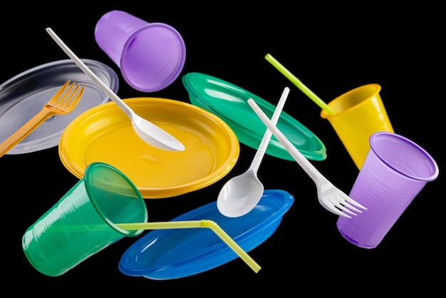 Flying multicolored disposable plastic tableware on a black background The concept of ecology and