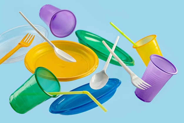 Flying multicolored disposable plastic tableware on a blue background The concept of ecology and r