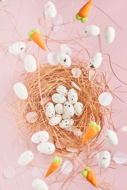 Flying quail eggs in nest and sweet carrot on pink table. Easter minimal creative vertical composition with copy space. Spring Happy Easter holiday  Top view.