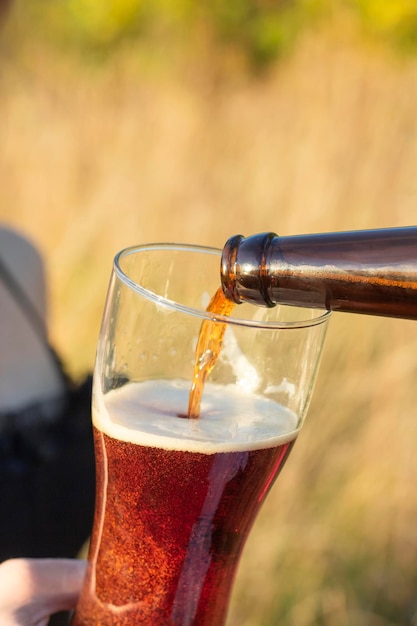 Foamy dark beer is poured into a glass glass in nature