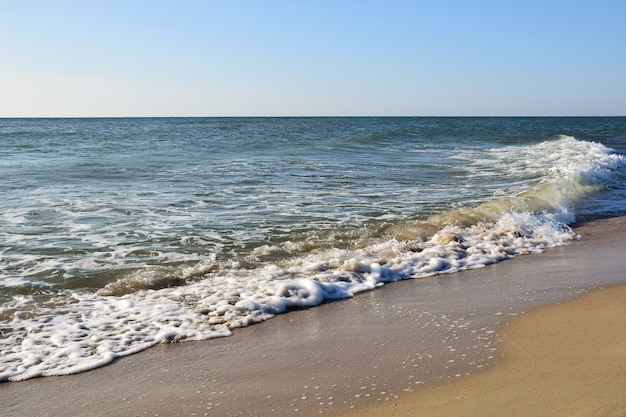 Foamy sea waves roll on the sandy daytime beach