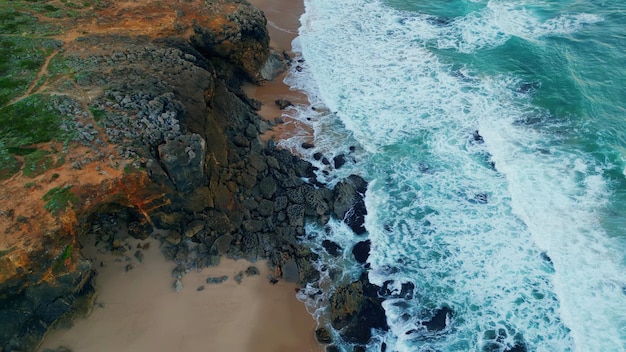 Foamy sea waves washing rocky seashore in slow motion aerial view stormy ocean