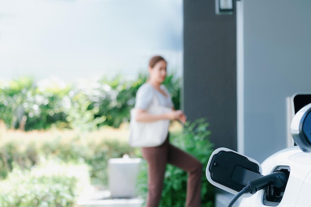 Focus charger plug into EV car with blur backdrop of progressive woman walking