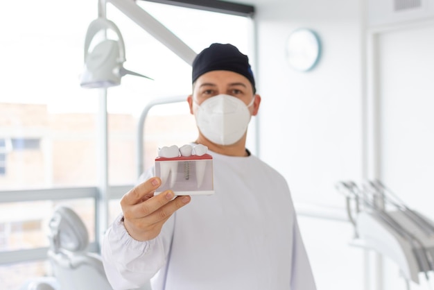 Focus on a dentist39s hand holding a dental implant model while his face is out of focus in the background Selective focus