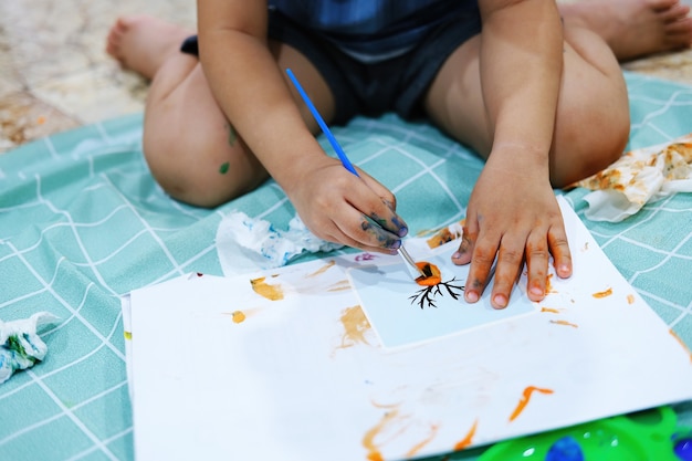 Focus on  hands on paper. Children use paintbrushes to paint watercolors on paper to create their imagination and enhance their learning skills.