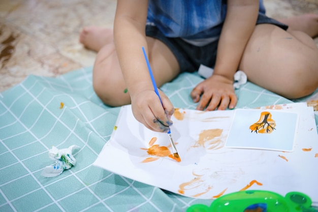 Focus on  hands on paper. Children use paintbrushes to paint watercolors on paper to create their imagination and enhance their learning skills.