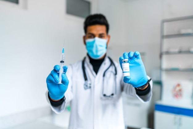 The focus is on the hand of the doctor who holds the injection and the coronavirus vaccine in his hand