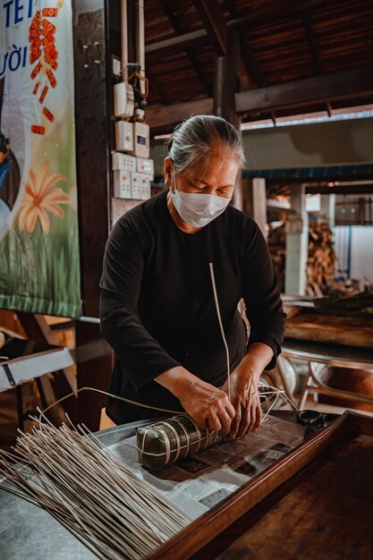 Focus old woman with traditional Vietnamese dress ao ba ba Making wrapping Tet Cake the Vietnamese lunar new year Tet food outdoor by hands