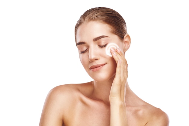 Focus on skin portrait of healthy young woman with closed eyes applying moisturizer cream on