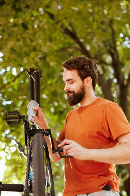 Focused and active man greasing and servicing modern bicycle chain for yearly summer maintenance Detailed image showing caucasian male skillfully lubricating bike pedals outdoors