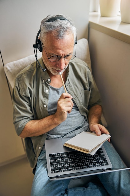 Focused aged man in glasses and headphones working from home