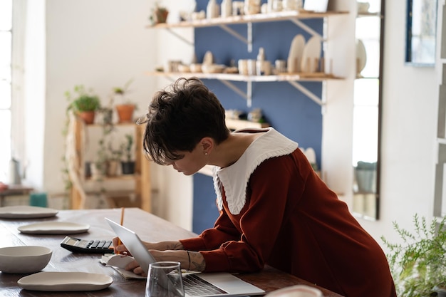 Focused artisan female pottery shop owner doing bookkeeping measuring small business profitability