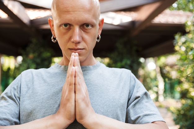 Focused attractive fitness yoga man meditating while standing outdoors