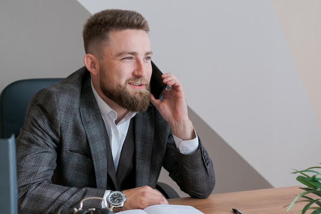 Focused bearded business guy in office clothes sitting at table and talking