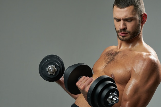 Focused bearded caucasian sportsman building up muscles with dumbbells in room indoors