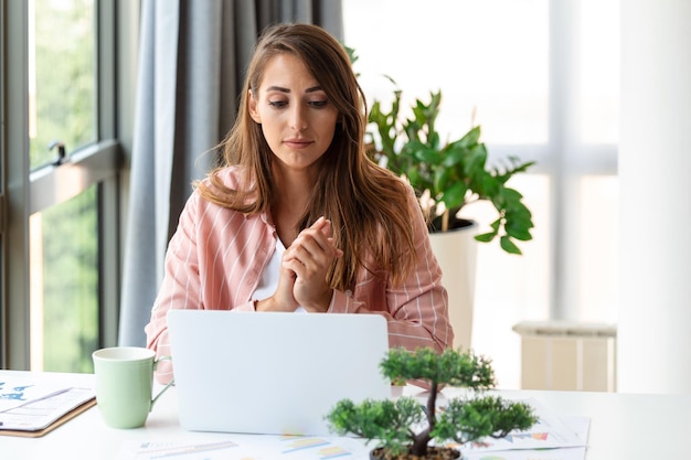 Focused business woman using laptop at home looking at screen chatting reading or writing email sitting on couch female student doing homework working on research project online