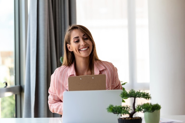 Focused business woman using laptop at home looking at screen chatting reading or writing email sitting on couch female student doing homework working on research project online