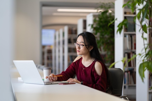 Focused chinese woman freelancer working remotely on laptop in public library or coworking