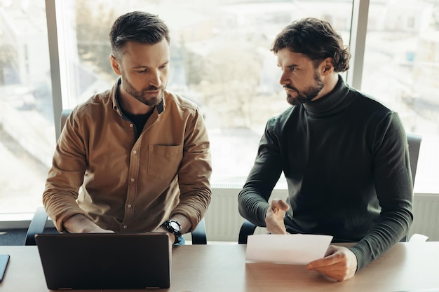 Focused company workers studying document collaborating using laptop at company office