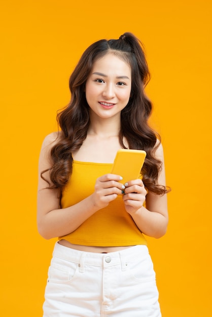 Focused curly woman texting message. Studio shot of elegant girl holding smartphone on yellow background.