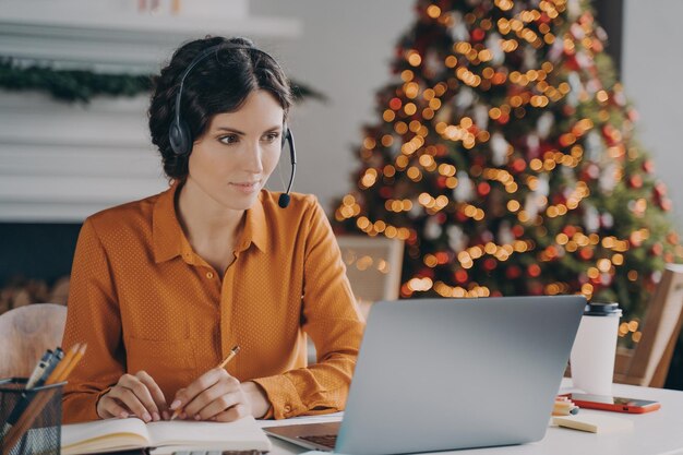 Focused European lady support consultant in headset with mic working at christmas time from home