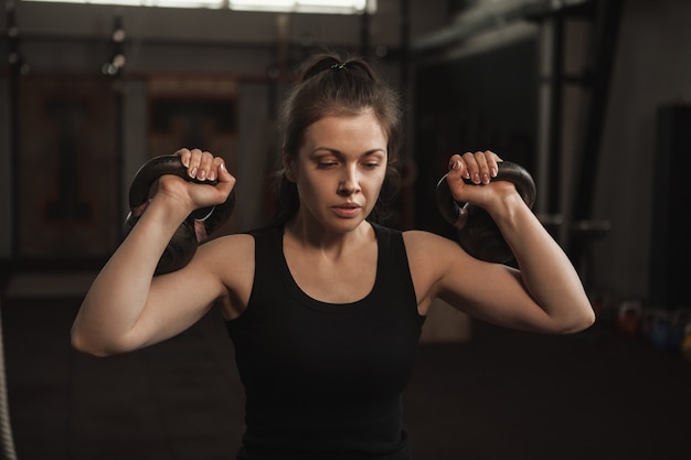 Focused female athlete exercising with kettlebells at the gym