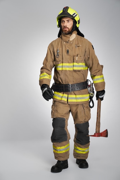 Photo focused firefighter in full gear with axe walking indoors front view of bearded fireman carrying