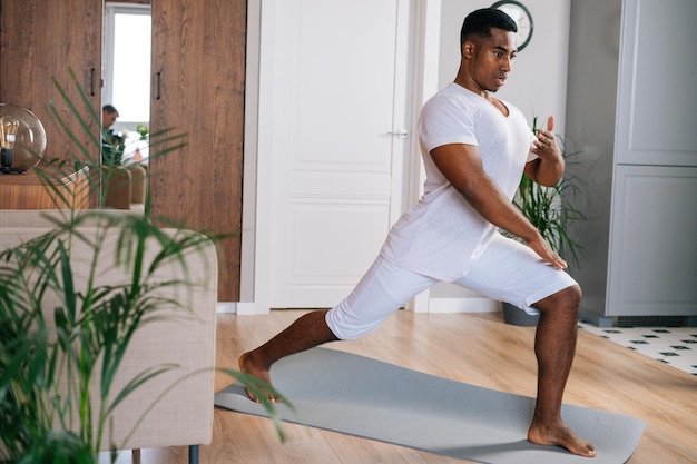 Focused fit AfricanAmerican man making sport fitness exercise standing on yoga mat