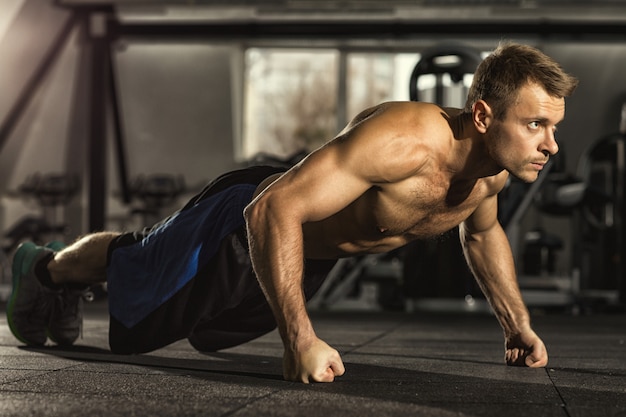 Focused handsome young strong sportsman doing pushups at the gym