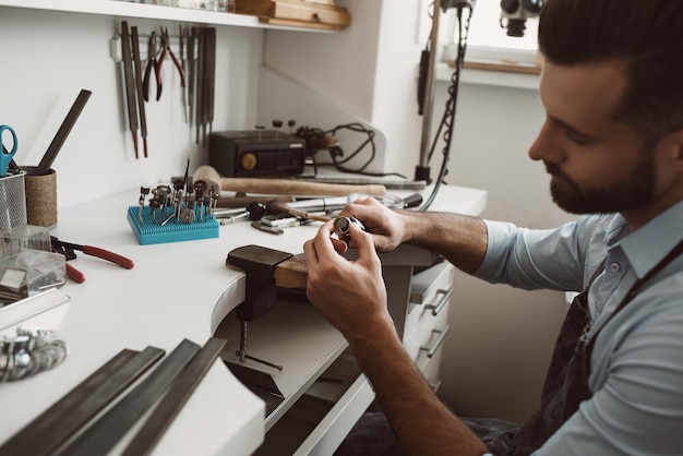 Focused on his work closeup photo of male jeweler making a new silver ring at