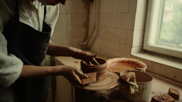 Focused lady working with wet clay in pottery Closeup serious ceramist using potters wheel in workshop Young woman making line on clay product in studio