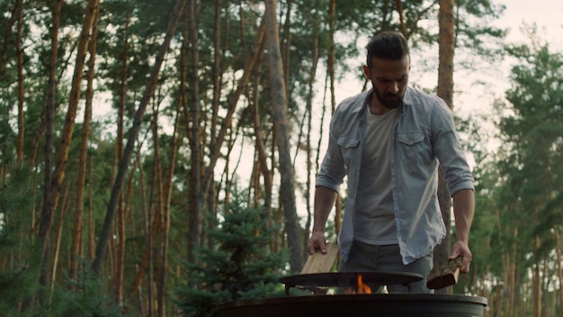 Focused man preparing fire for bbq outside Man chef putting firewood in grid