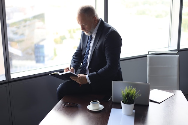 Focused mature businessman working and taking notes in his modern office.