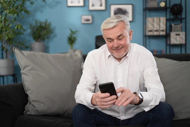 Focused middle aged grandfather resting on sofa web surfing healthcare information on digital