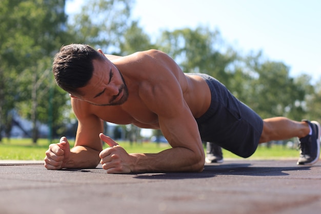 Focused muscular guy doing plank exercise outdoors.