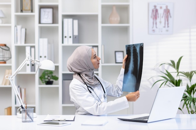 Focused muslim woman doctor with stethoscope checking xray of lungs while sitting at hospital