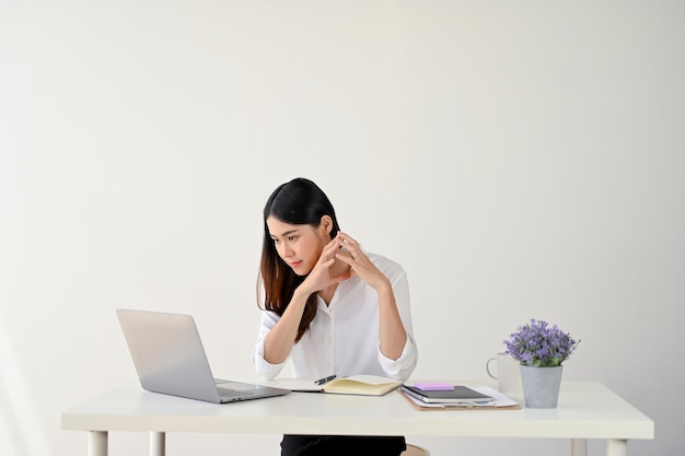 Focused and serious Asian businesswoman working on her assignment on her laptop at her desk