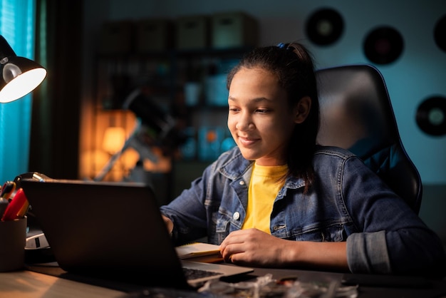 Focused smiling teen uses laptop at home looking at screen chatting reading or writing email