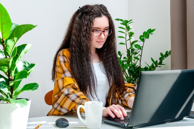 Focused woman in glasses typing on laptop keyboard is working at home writing emails online shopping