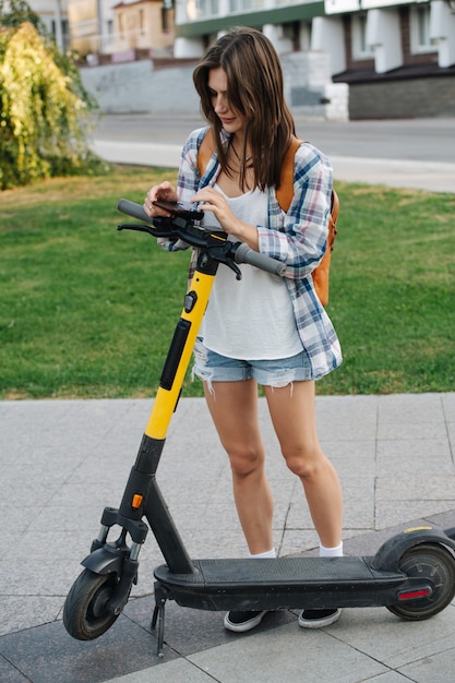 Focused woman in the park paying for her electric scooter with a phone app