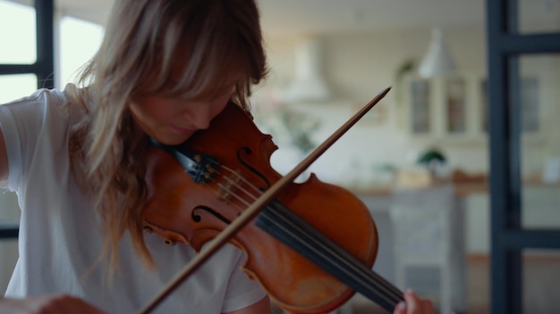 Focused woman playing violin in living room Teenage girl creating music on string instrument in living room Portrait of female musician using violin bow Violinist playing chords on instrument