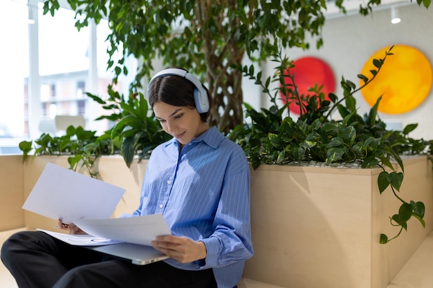 Focused woman in the wireless headphones holding papers in her hands in a coworking space