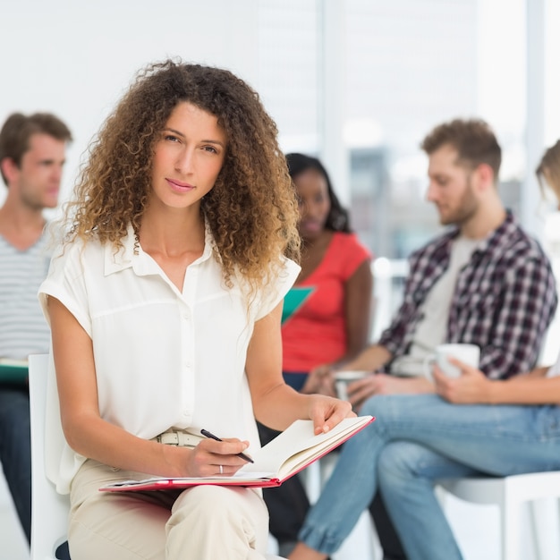 Focused woman writing while colleagues are talking behind her