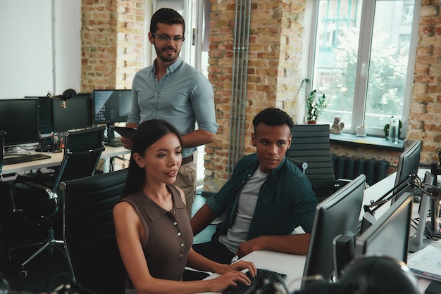 Focused on work group of young employees looking at computer monitor and discussing something while