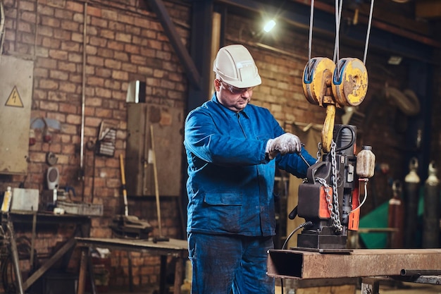 Focused worker is using a small mobile drill to make a holes in the part of rail.