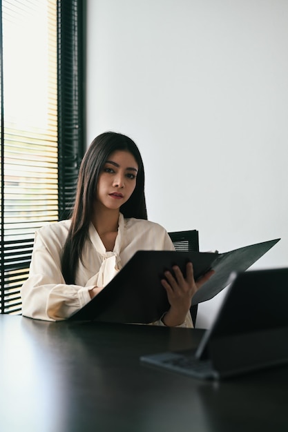 Focused young businesswoman analyzing investment data documents on wooden office desk